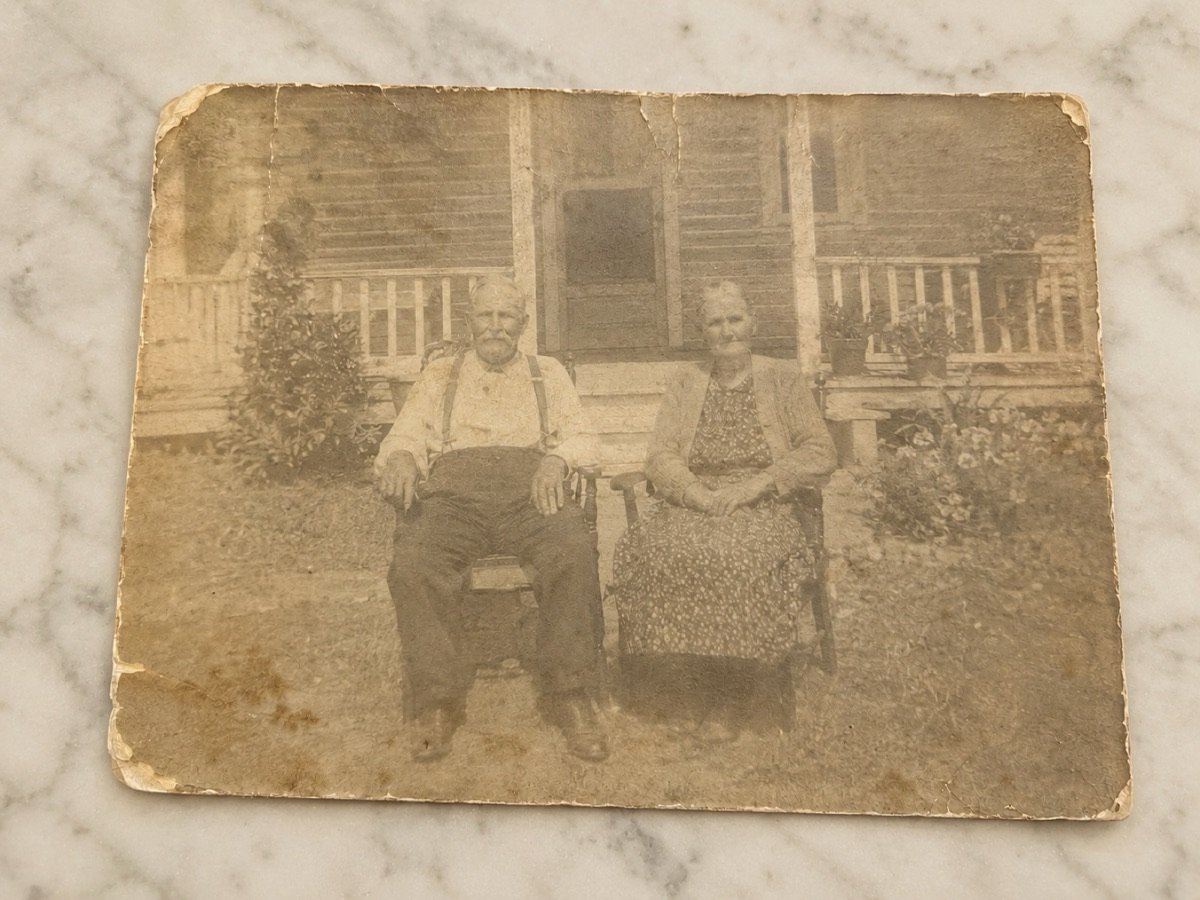 Foto original: pareja de ancianos sentados frente a la casa de la familia